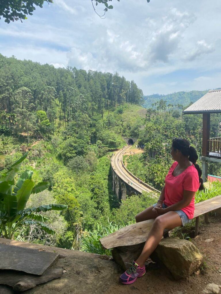 Ola, founder of Ola World, sitting on a wooden bench overlooking the iconic Nine Arch Bridge in Sri Lanka — a symbol of her journey as a curious traveler