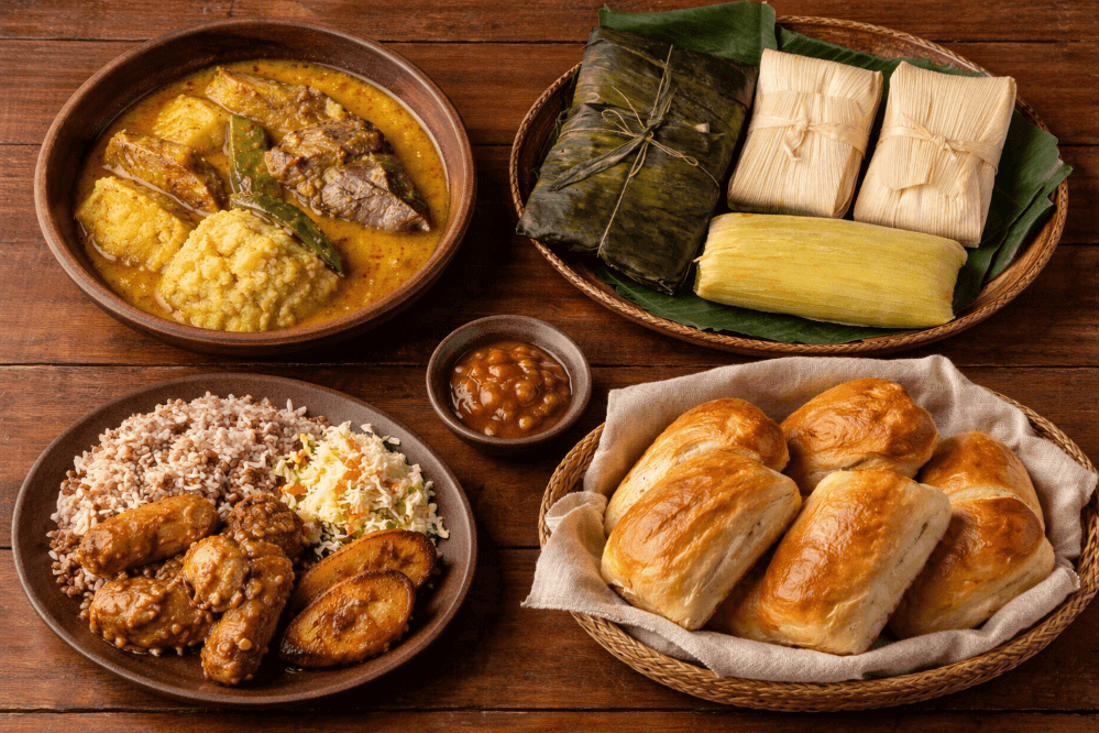 Traditional food in Belize: hudut, tamales, rice and beans, and coconut bread on wooden table