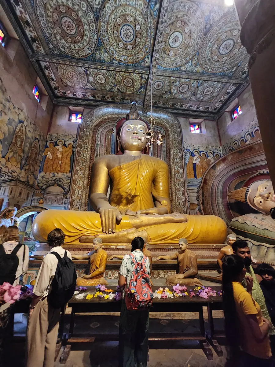 Worshippers laying flower trays before a large golden Buddha inside the image house of a Buddhist temple in Sri Lanka