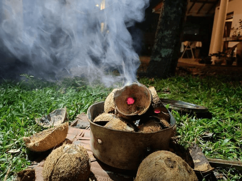 Coconut shells burning in a metal pot with glowing embers and smoke — perfect for grilling outdoors