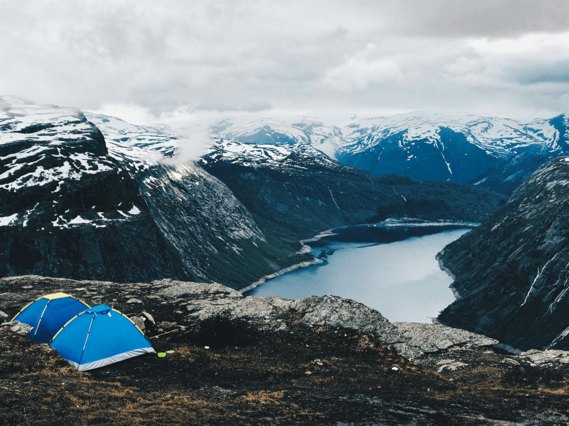 Eco-camping in the USA: blue tents on a rocky ridge overlooking a fjord and snow-capped peaks — low-impact travel at its most dramatic