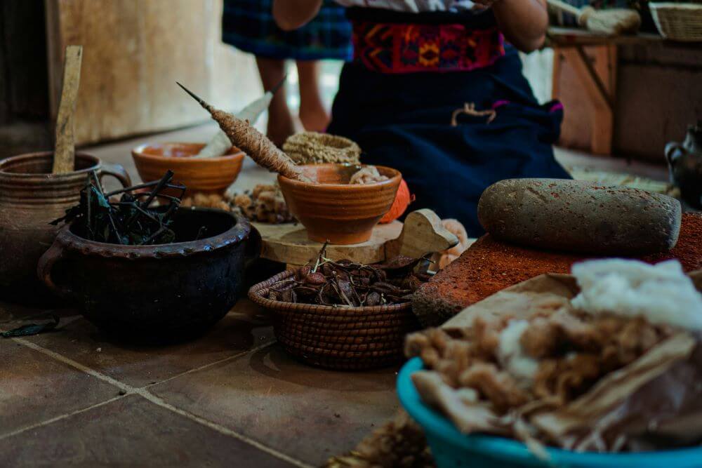 A traditional Guatemalan home cooking table: black beans, handmade corn tortillas, fresh salsa, avocado, and a stone metate for grinding masa — the daily meal of Maya and mestizo families.