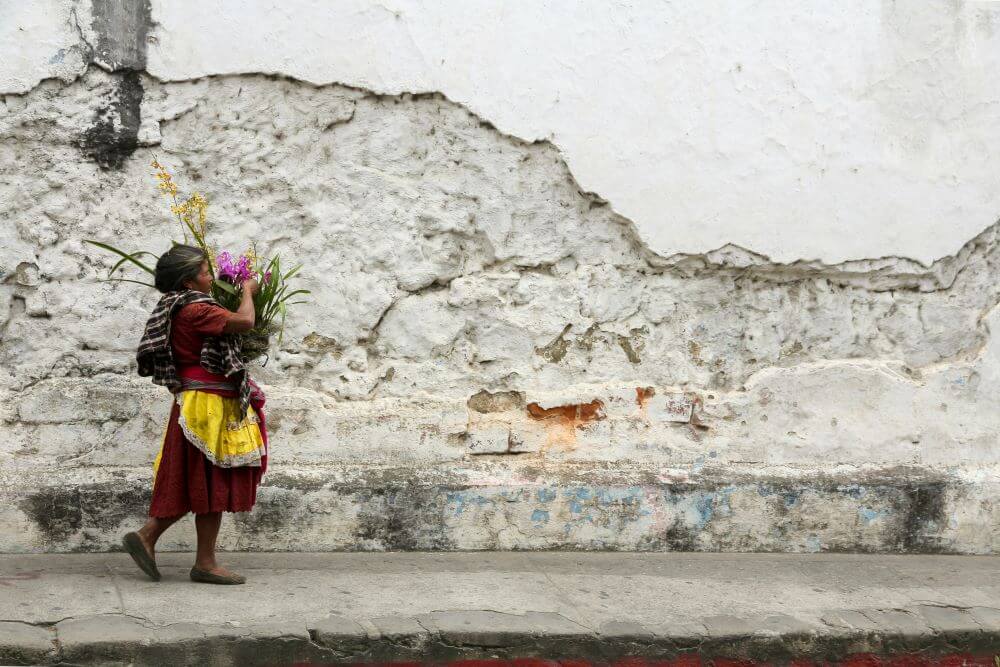 A Guatemalan woman in traditional attire walking through a village market — a living link to Maya foodways and community life