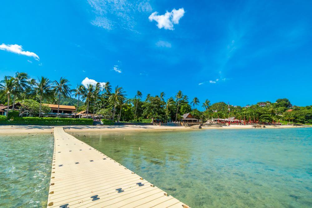 Public beach in Seychelles with wooden walkway, turquoise water, and granite boulders — no resort access required