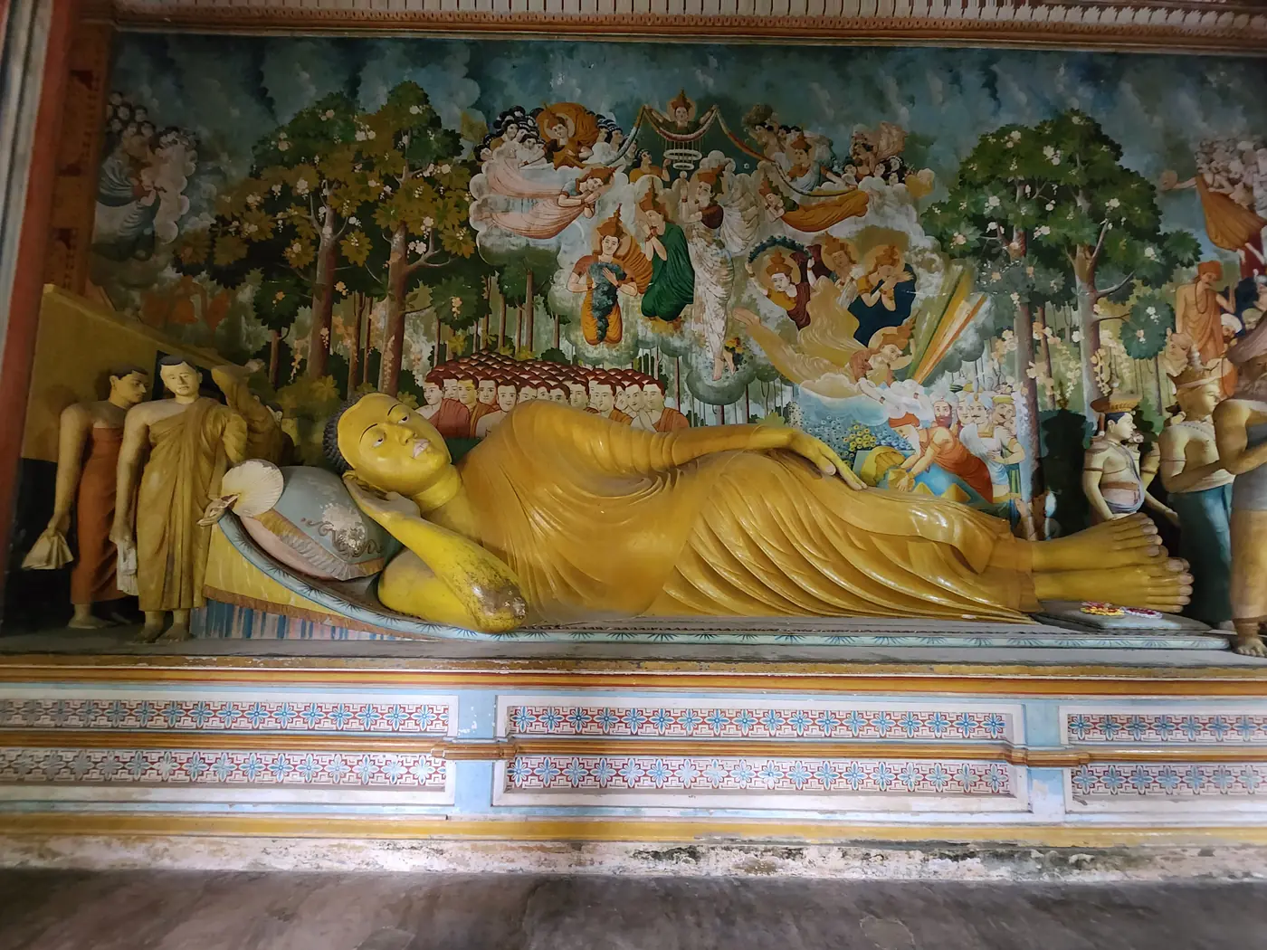 Reclining Buddha statue with painted wall murals inside a Sri Lankan cave temple
