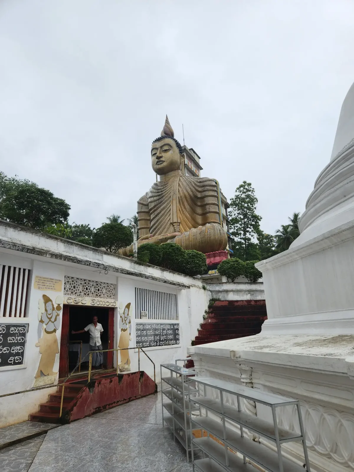 A white dagoba stupa beside a giant Buddha statue at a Sri Lankan Buddhist temple