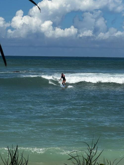 Surfer riding a wave from shore view — shows stability and flow of a longboard or funboard in moderate conditions